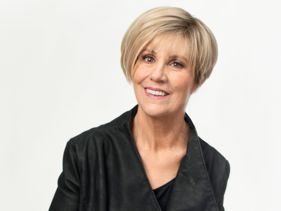 Headshot of an older Caucasian woman with short blond hair parted to the side smiling at the camera wearing a black blazer.