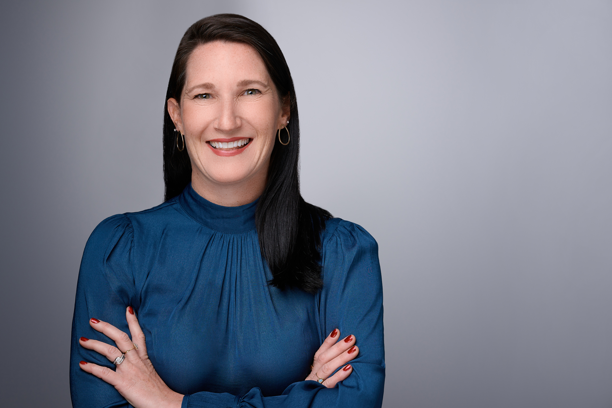 Portrait of a smiling woman with dark hair and arms crossed.