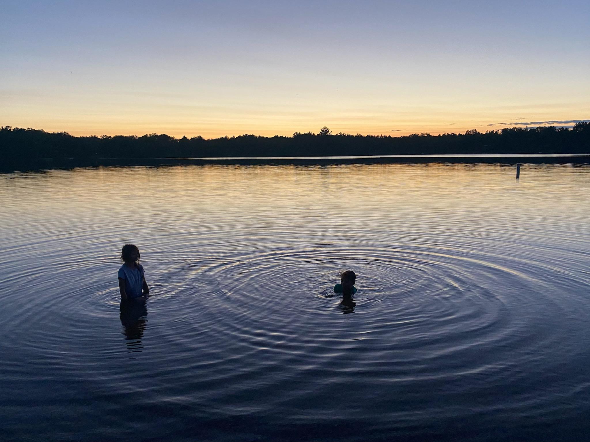 Two children in a calm lake at dusk.
