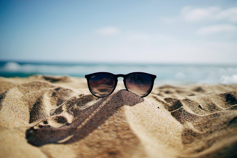 sunglasses on beach with water behind them
