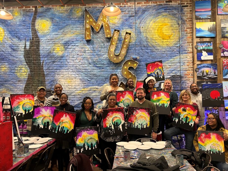 ASMG team holding up their paintings of a sunset over the city.