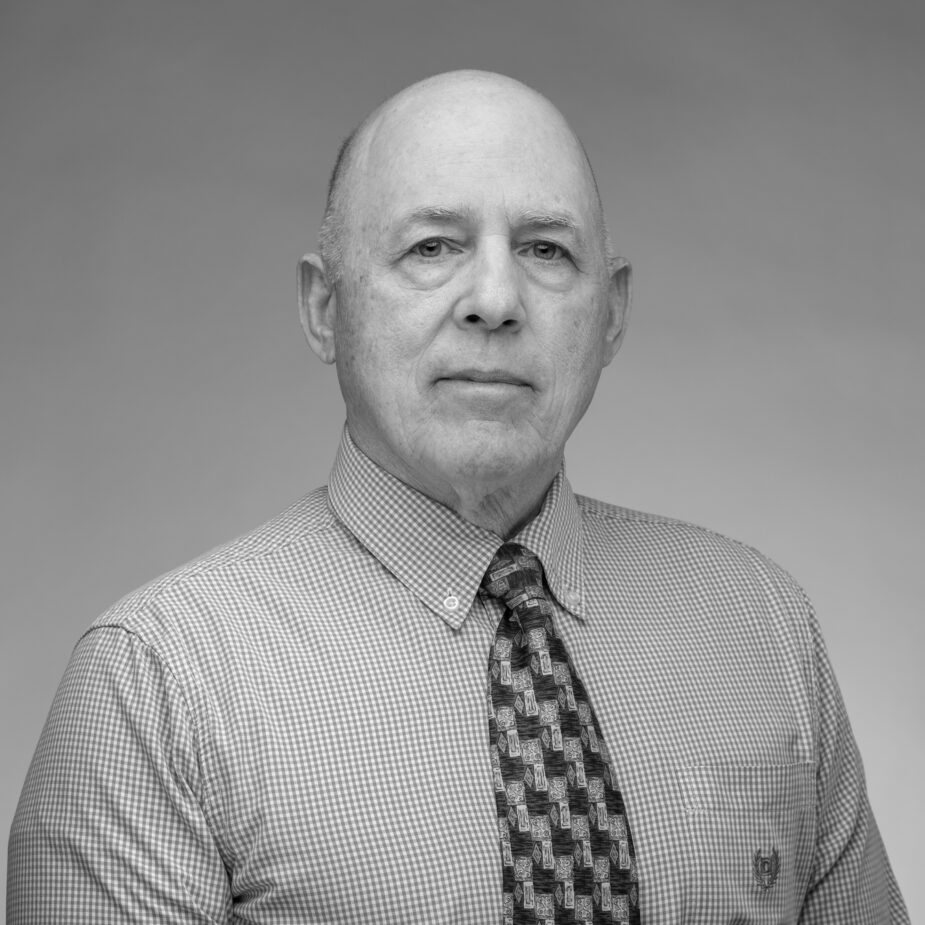Black and white headshot of a bald older Caucasian male wearing a button up and tie.