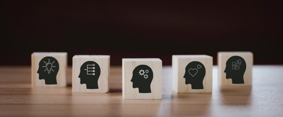 Five wooden blocks painted with a side profile of a black head facing left. On the brain portion of the head there are different symbols representing teamwork, creativity, and relationships.