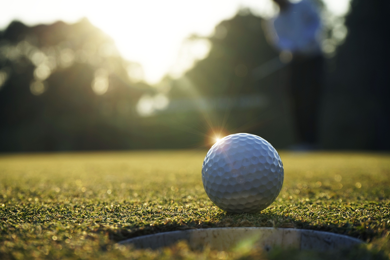 A golf ball reflecting the sun on the green sitting near the hole.