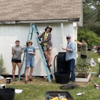 CEO Jim O'Farrell smiling for the camera with Arcadia interns while painting a shed.