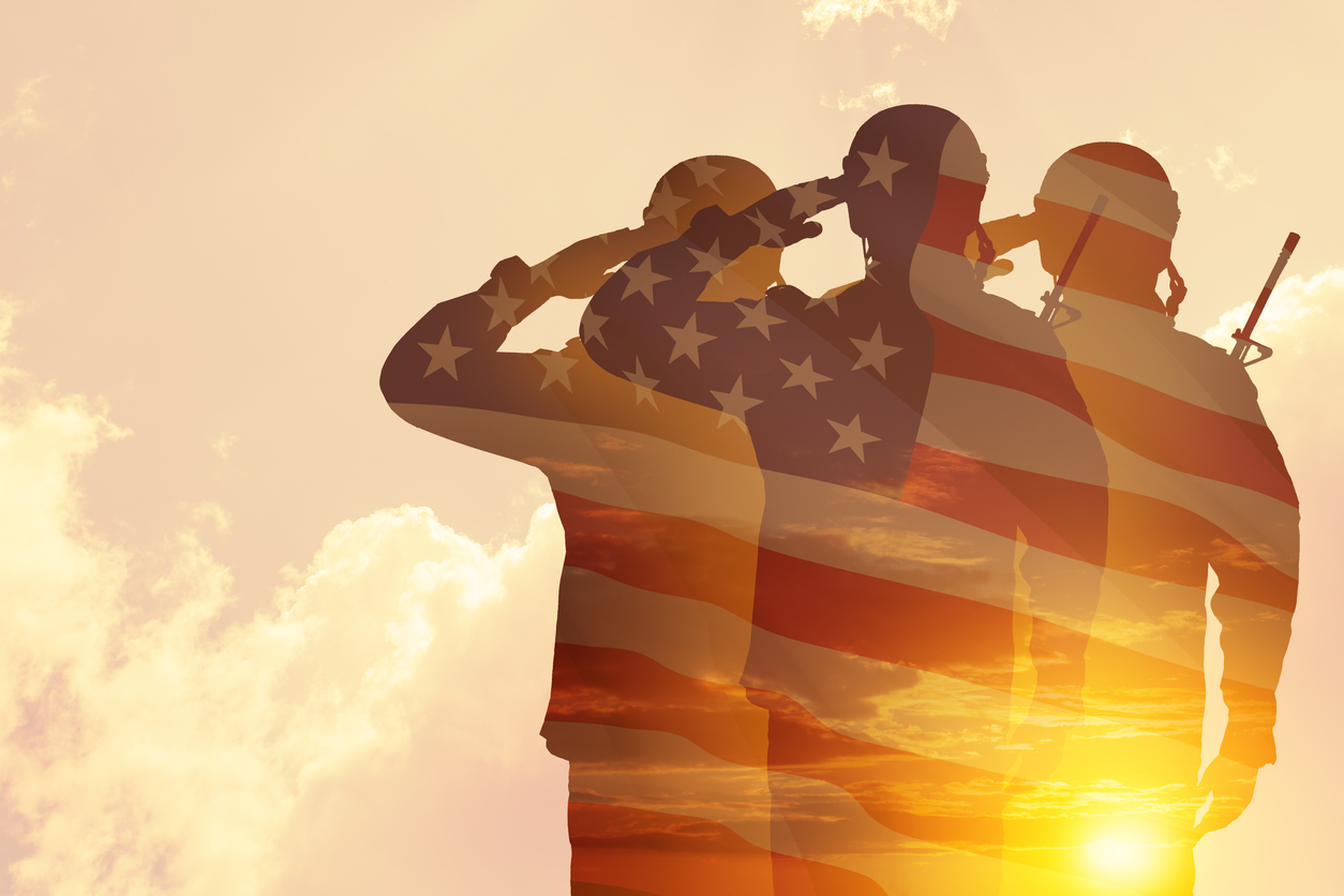 Silhouettes of three soldiers saluting, overlaid with an American flag pattern, against a sunset background with clouds.