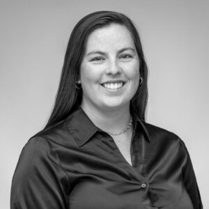 Black and white headshot of a young Caucasian woman with long hair and a button up blouse smiling at the camera.