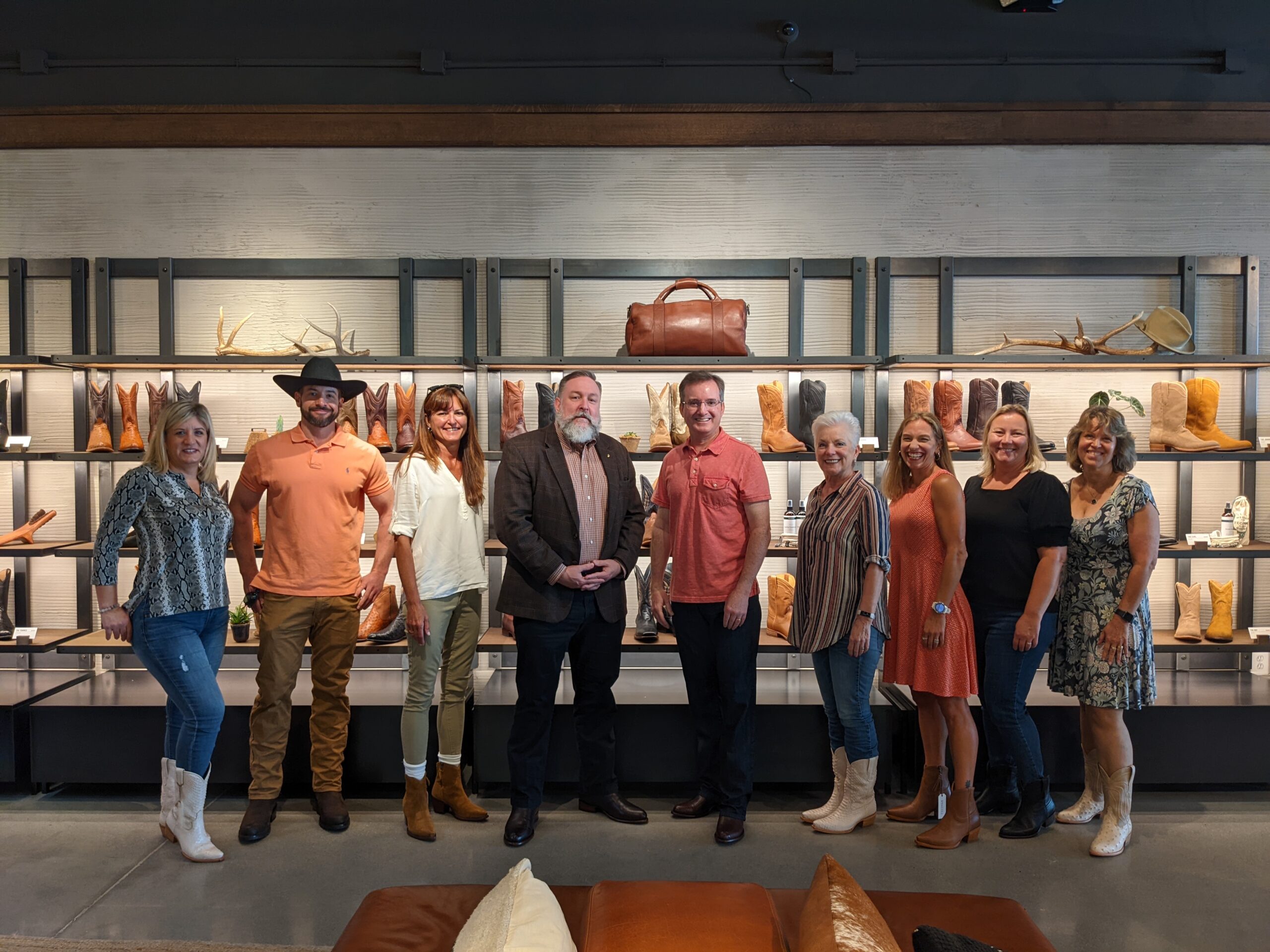 A group of eight adults standing in front of a display of boots and leather goods.