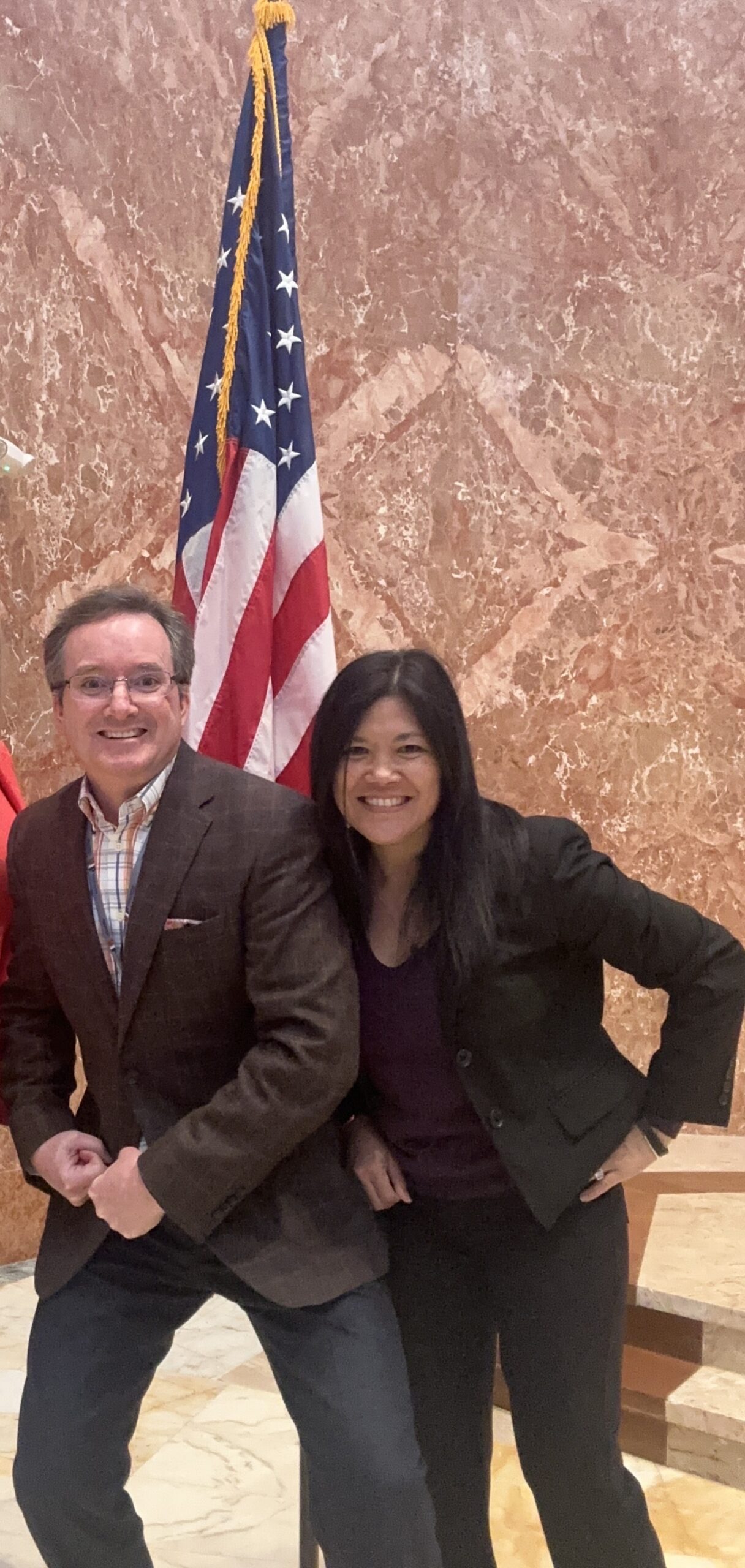 Two smiling adults striking a playful pose in front of an American flag.