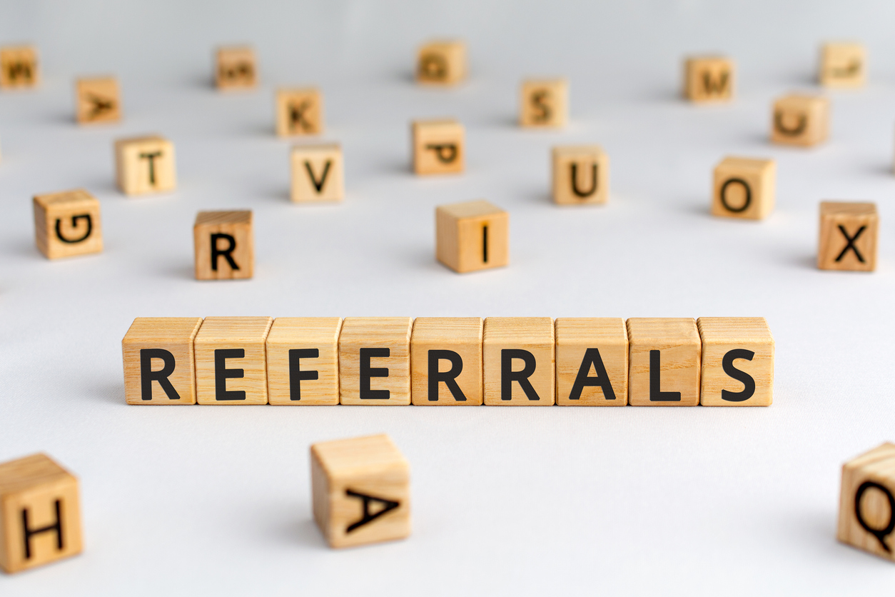 Wooden blocks spelling "REFERRALS" with scattered letter blocks on a white surface.