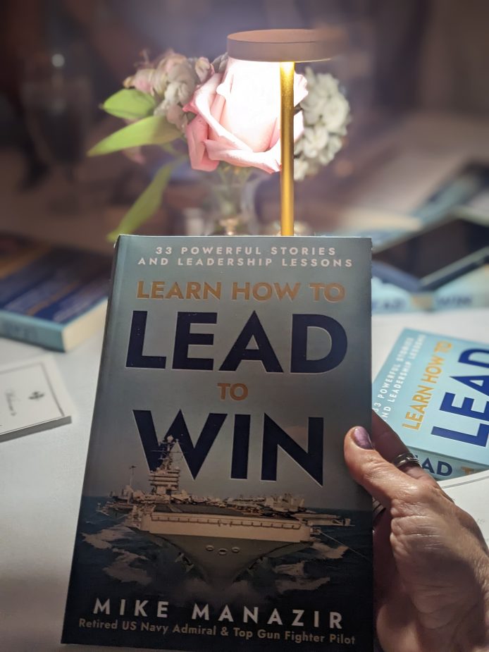 Woman holding a book titled "LEARN HOW TO LEAD TO WIN".