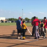 A group of young softball players and adults stand on the infield of a softball field during daylight.
