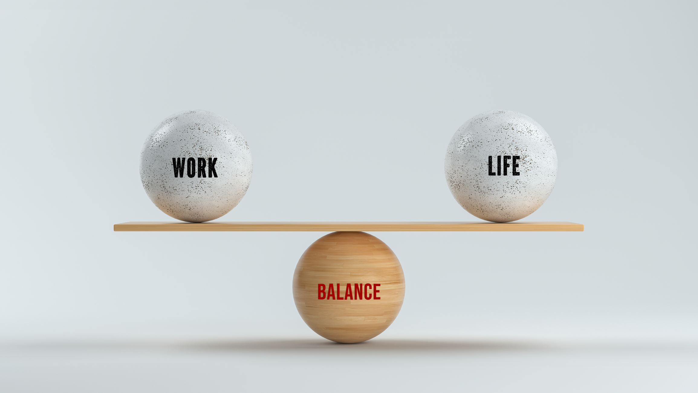 A conceptual 3D rendering of a wooden balance scale perfectly centered on a wooden base. The scale holds two identical white, speckled spheres, one labeled "WORK" and the other labeled "LIFE," demonstrating perfect equilibrium. The base is labeled "BALANCE" in red.
